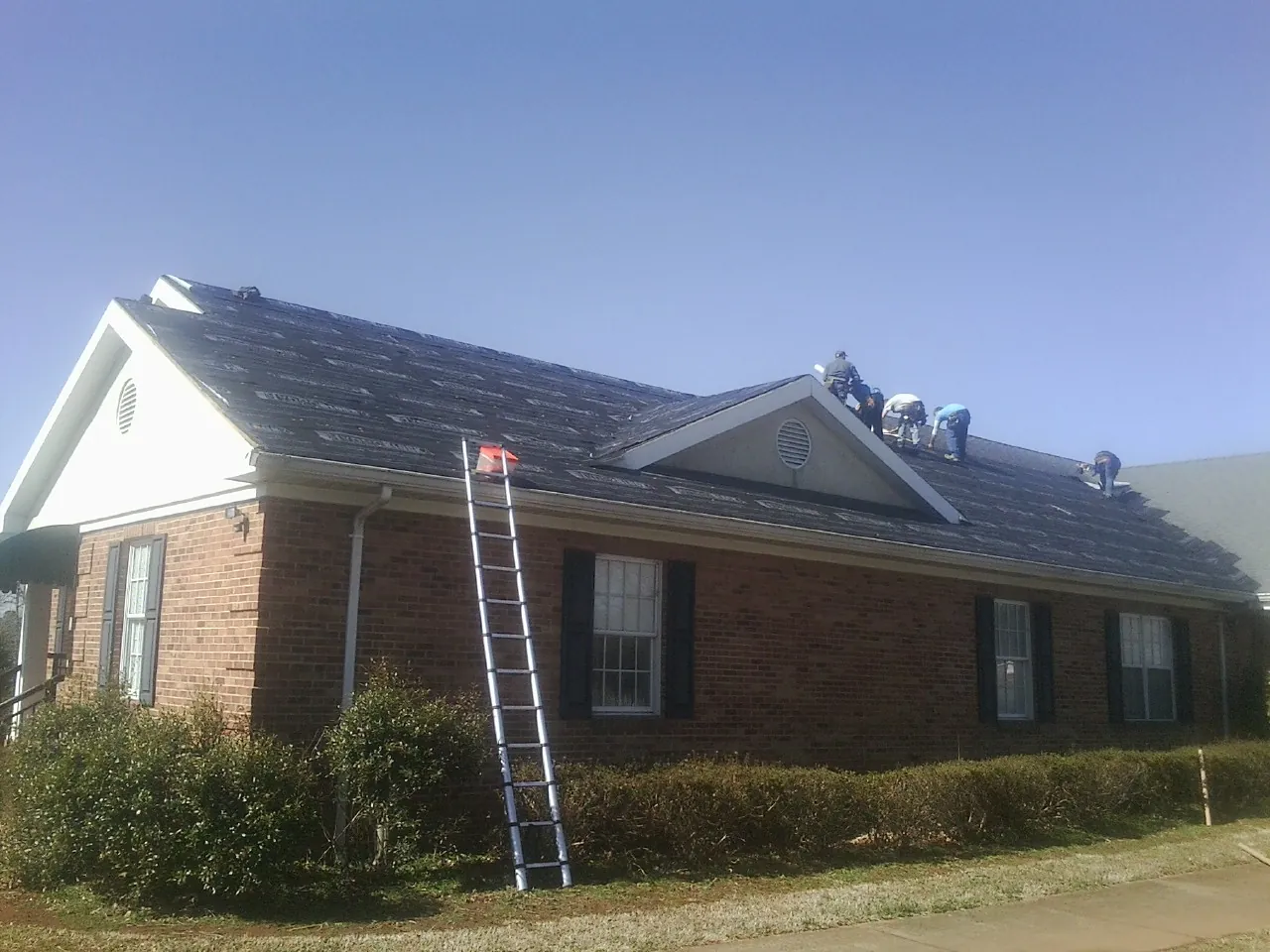 Crew tearing shingles off a brick ranch roof with a ladder set — Emergency Roof Repair work by our crew in Congers