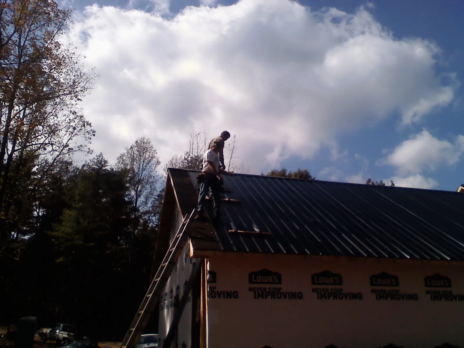 Roofer fastening dark metal panels high against a cloudy sky, from a Roof Inspection job in Congers