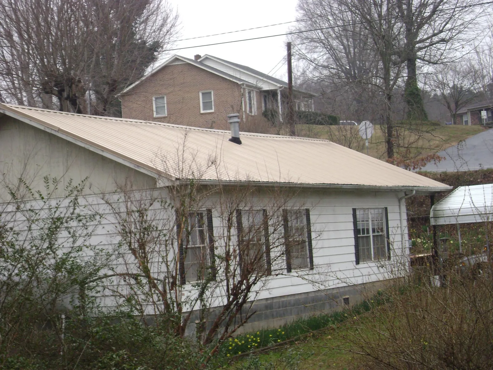 Tan metal roof on a white sided house set into a hillside — Commercial Roofing by Roofing Brothers in Congers